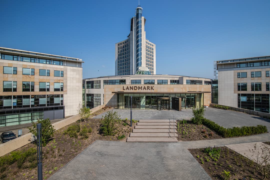A modern building complex with "LANDMARK" on the entrance, featuring a central tower and two adjacent wings under a clear blue sky.