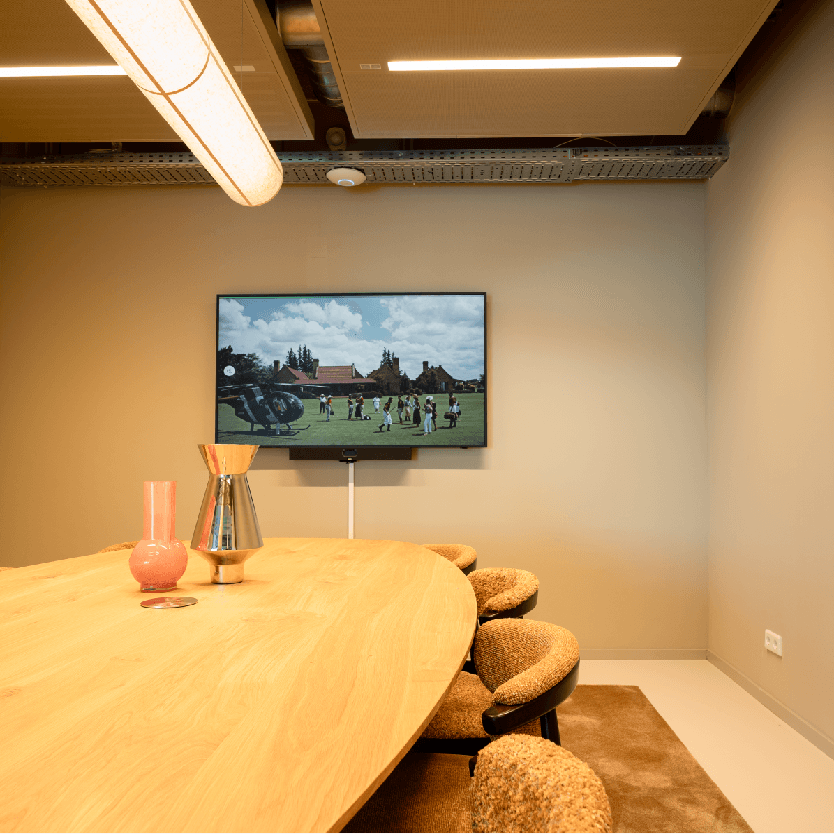 Modern conference room with a wooden table, plush chairs, decorative vases, and a wall-mounted TV displaying a golf scene.